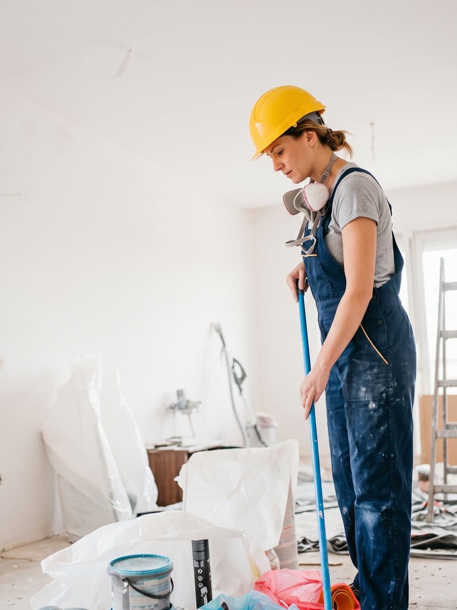 Worker in a hard hat sweeping debris in a room under renovation