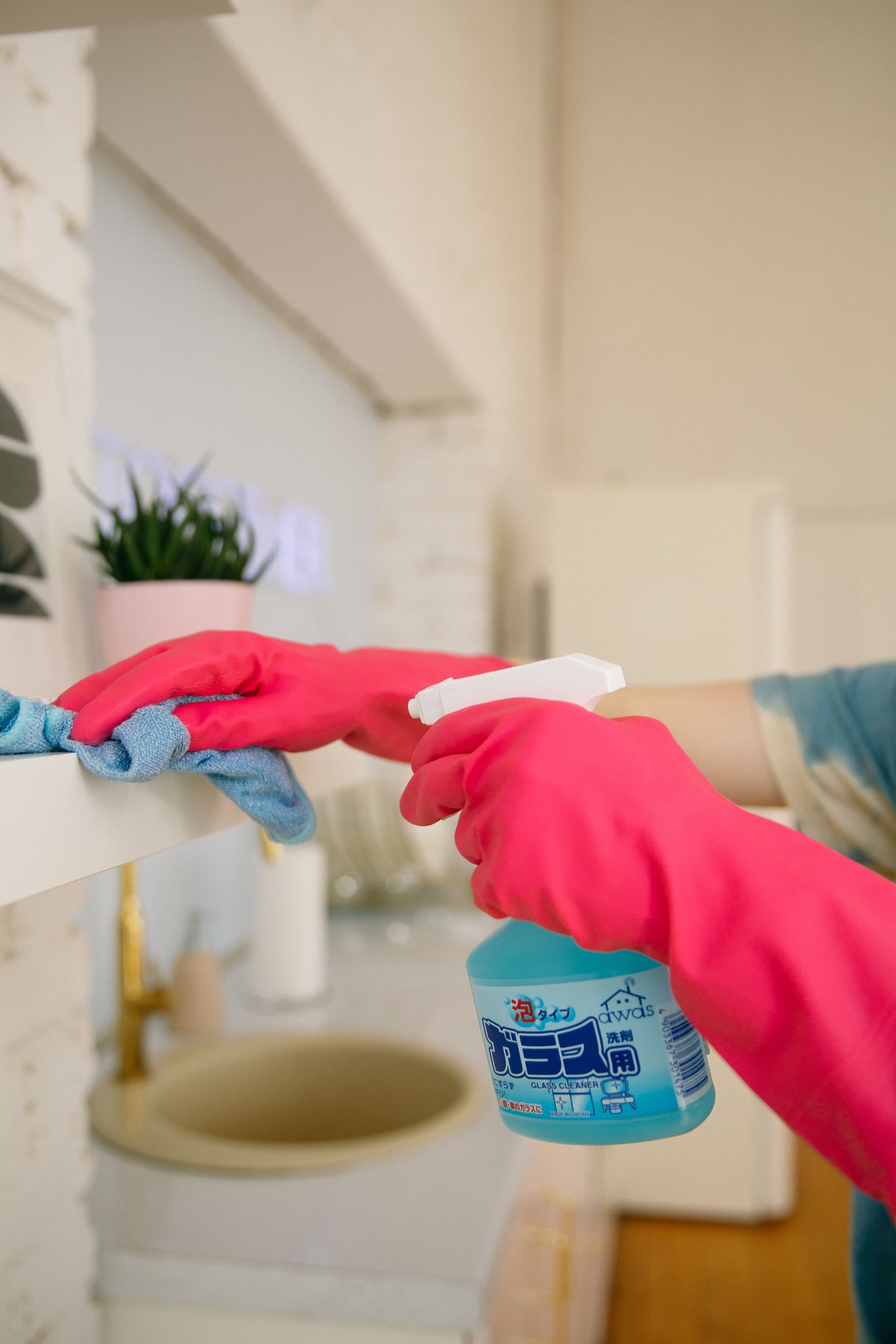 Gloved hands wiping a bathroom shelf with spray cleaner